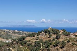 A coastal landscape with scattered buildings, a clear sky, and distant mountains.