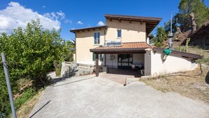 A two-story house with a tiled roof, a covered patio, and a garden with trees and shrubs.