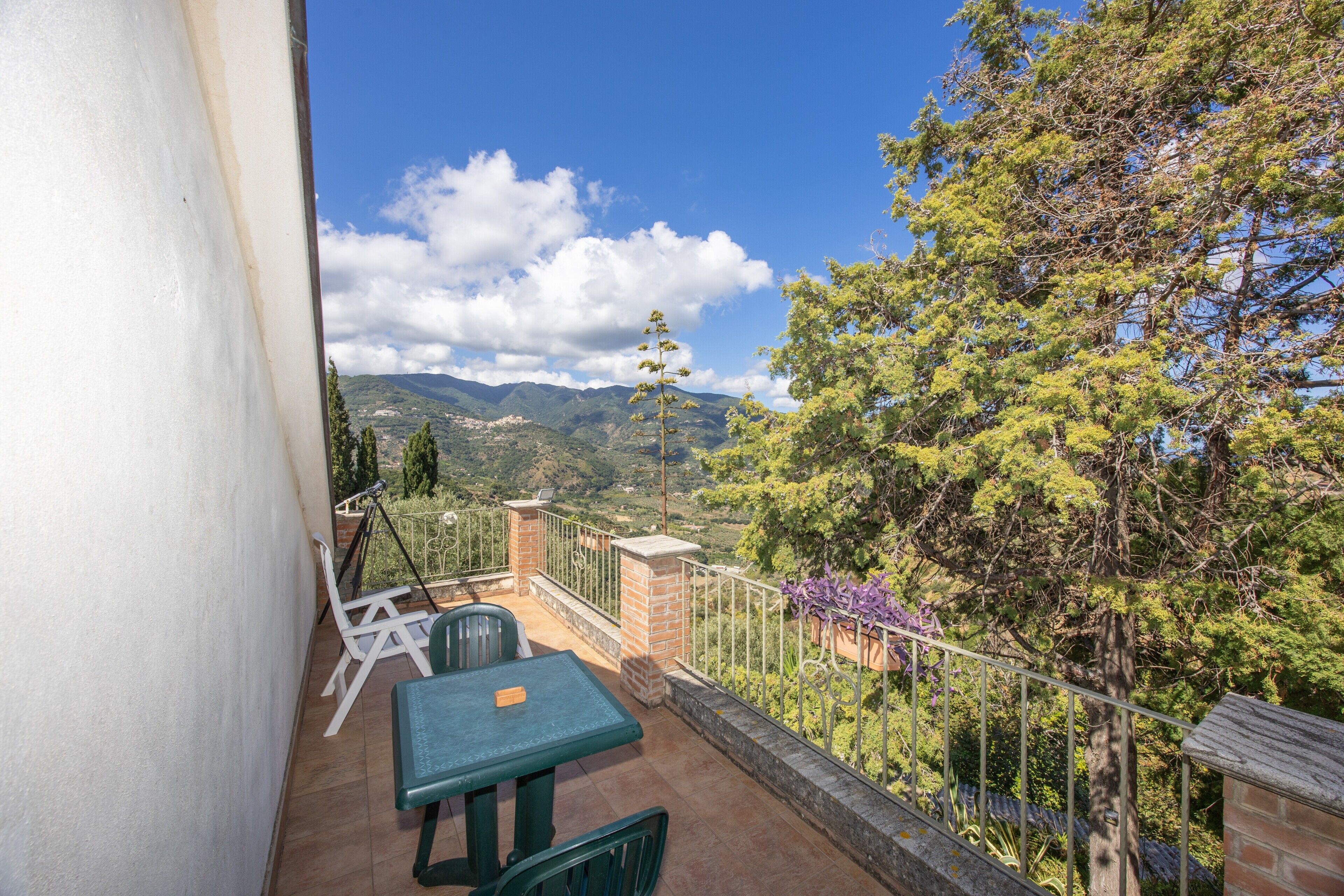 A balcony with a table and chairs, a view of mountains, and a railing.