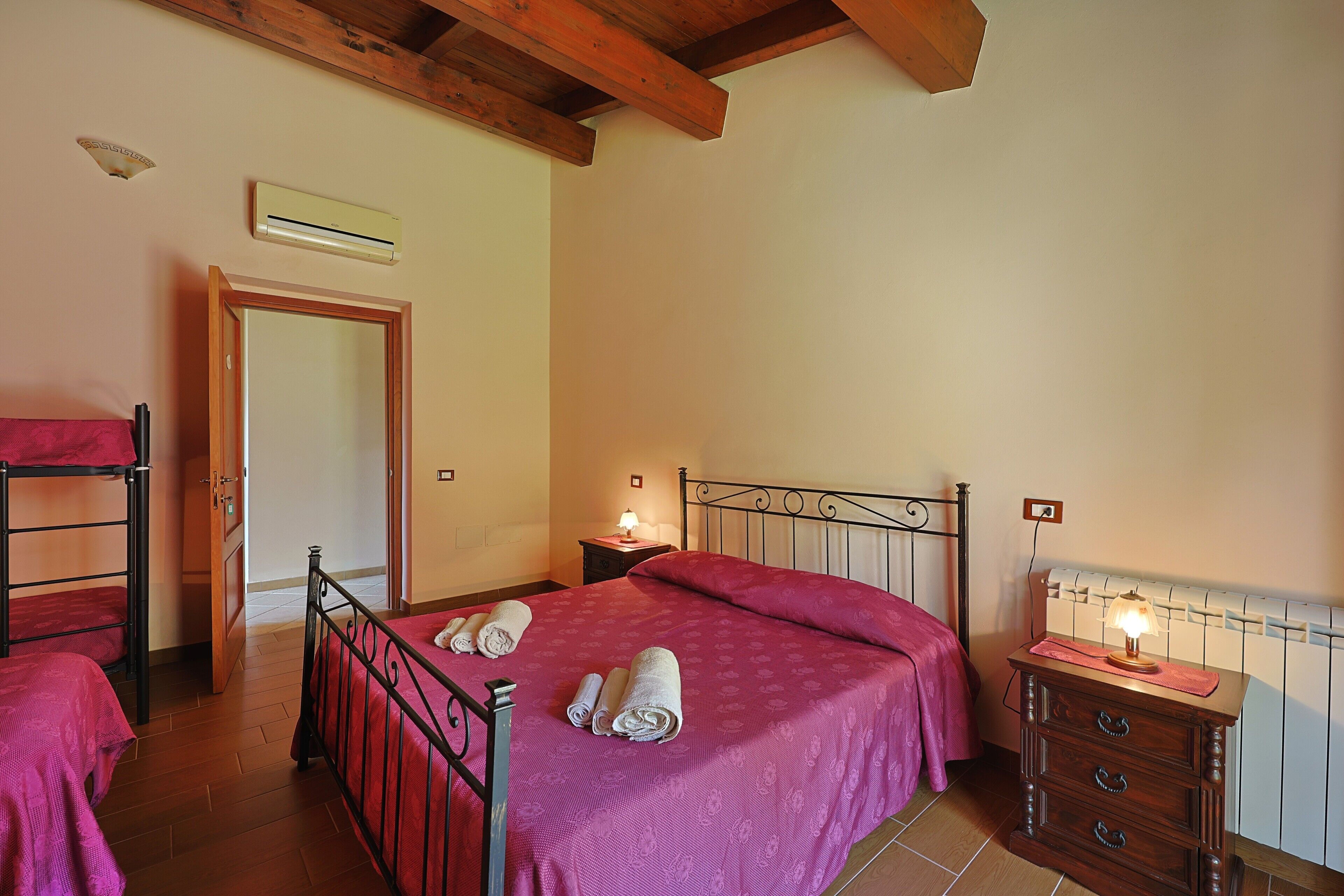 A bedroom with a bunk bed, a single bed with a pink bedspread, a nightstand with a lamp, and a dresser with drawers.