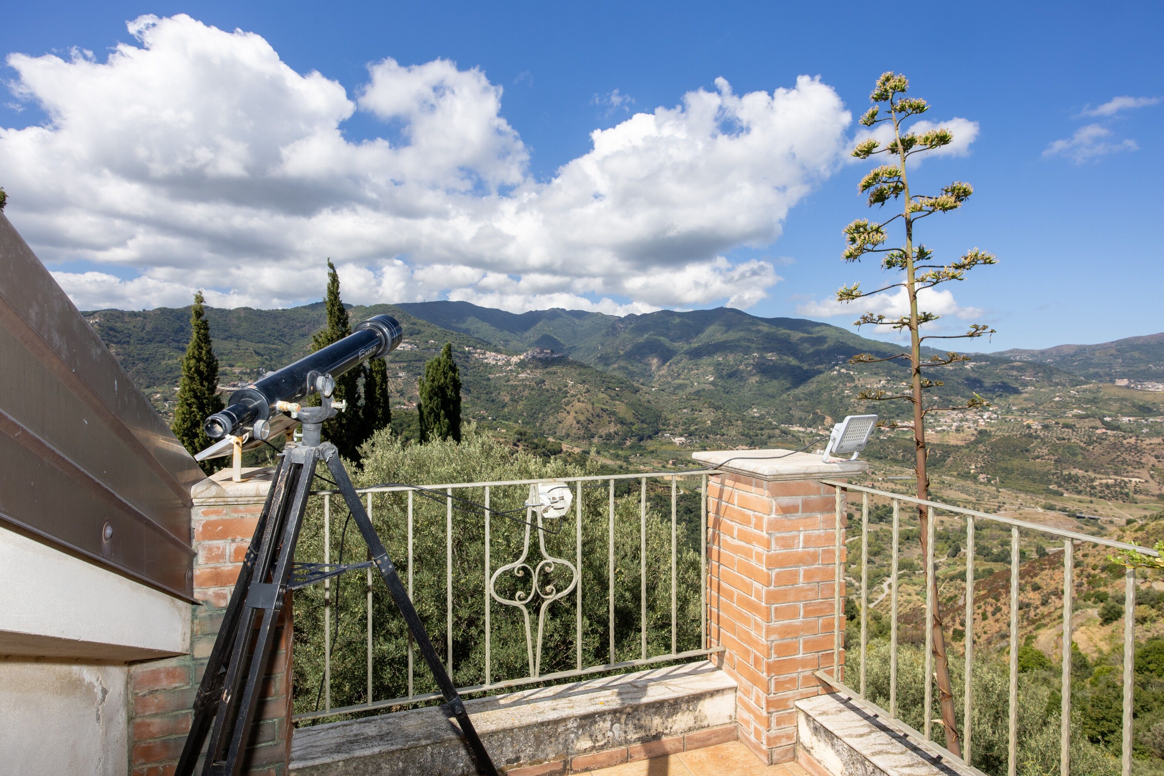 A balcony with a telescope, a brick wall, and a view of mountains.