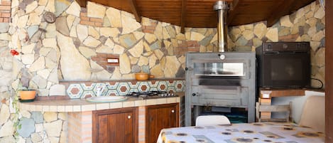 A stone and brick kitchen with a built-in oven and a television.