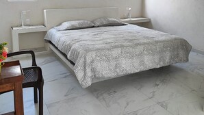 Un dormitorio con cama, escritorio, silla, ventilador de techo y dos ventanas con persianas.