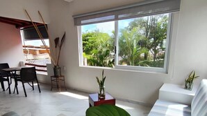Una sala de estar moderna con un ventanal grande, un sofá, un comedor y una planta.