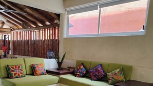 Una habitación con sofá verde, techo de madera, ventana grande y suelo de baldosas.