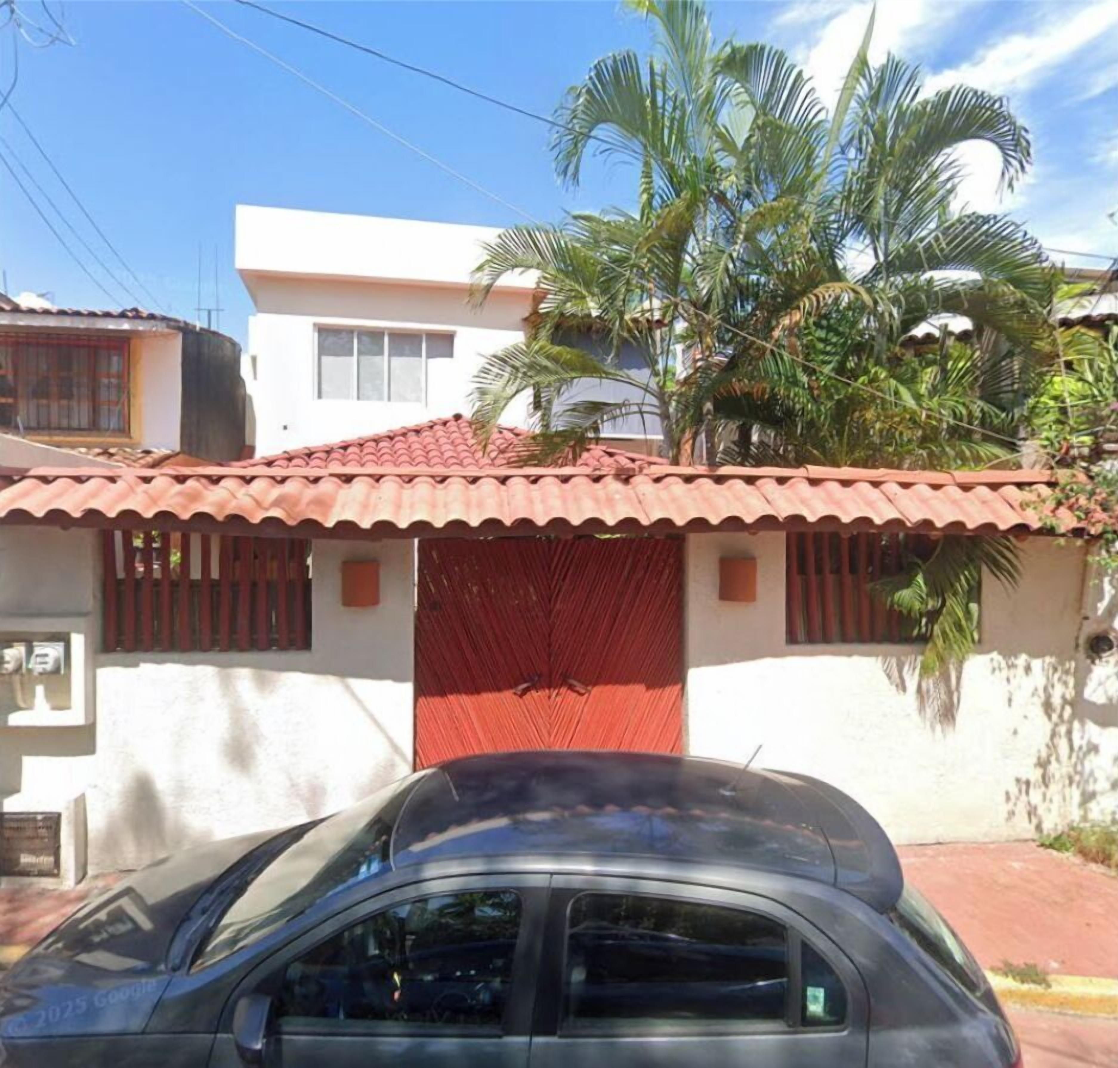 Un edificio residencial con techo de tejas rojas, entrada con portón y un coche estacionado en la parte delantera.