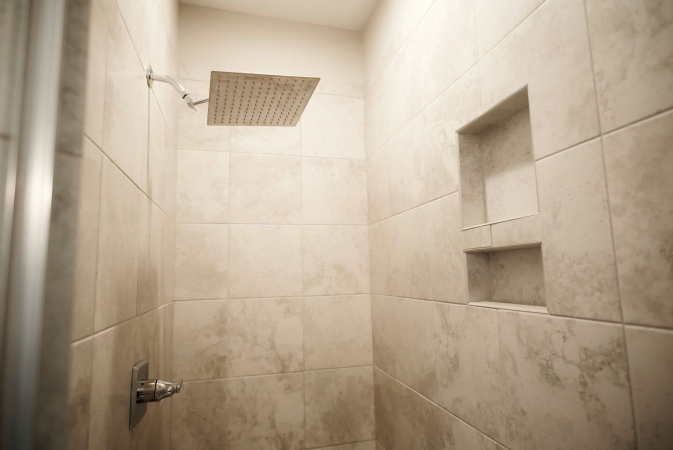 Een douche met een vierkante douchekop, betegelde wanden en een inbouwkastje.