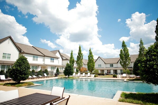 A pool area with lounge chairs and a building with multiple windows.