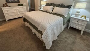 Ein Schlafzimmer mit einem großen Bett, einem Schminktisch, einem Nachttisch und einer Lampe.