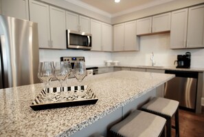A kitchen with a granite countertop, stainless steel appliances, and a tray with wine glasses.