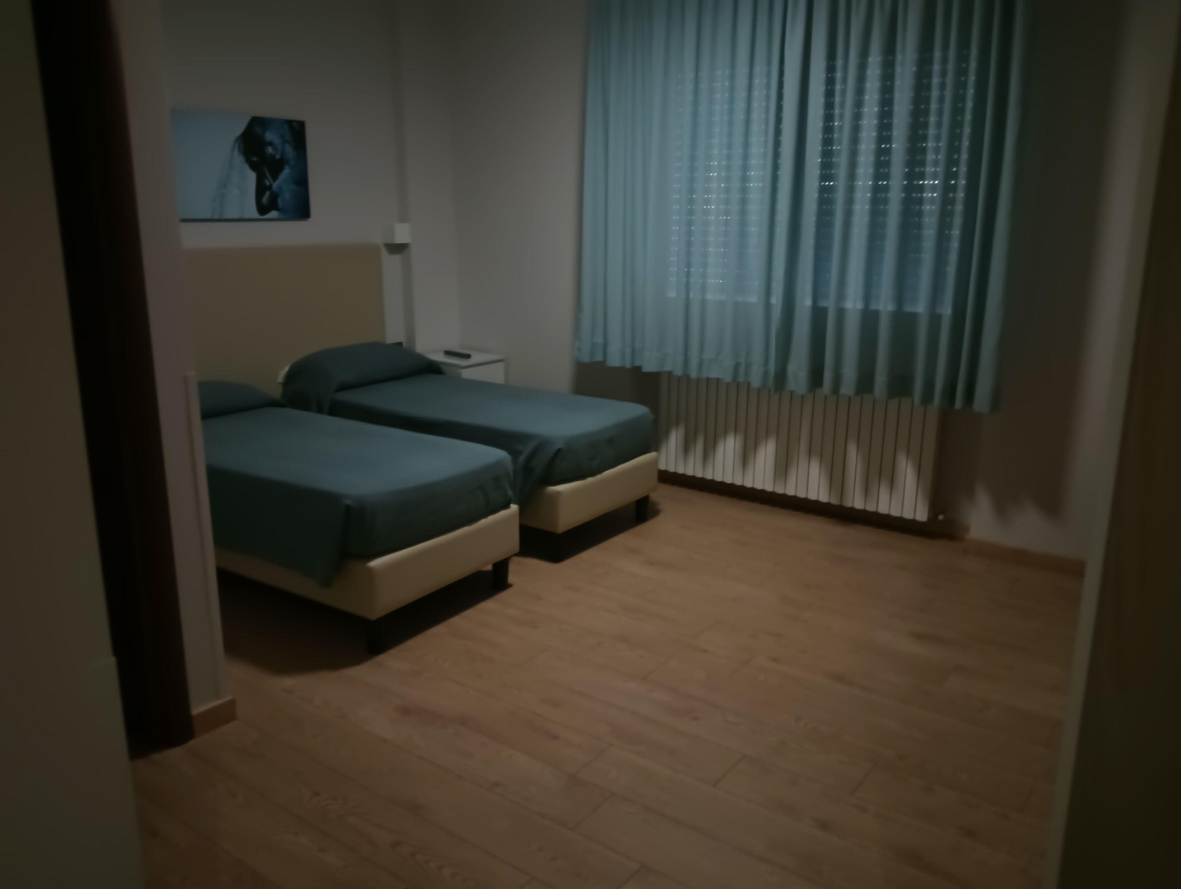 Un dormitorio con dos camas, una mesita de noche, una lámpara de pared y una ventana con cortinas.