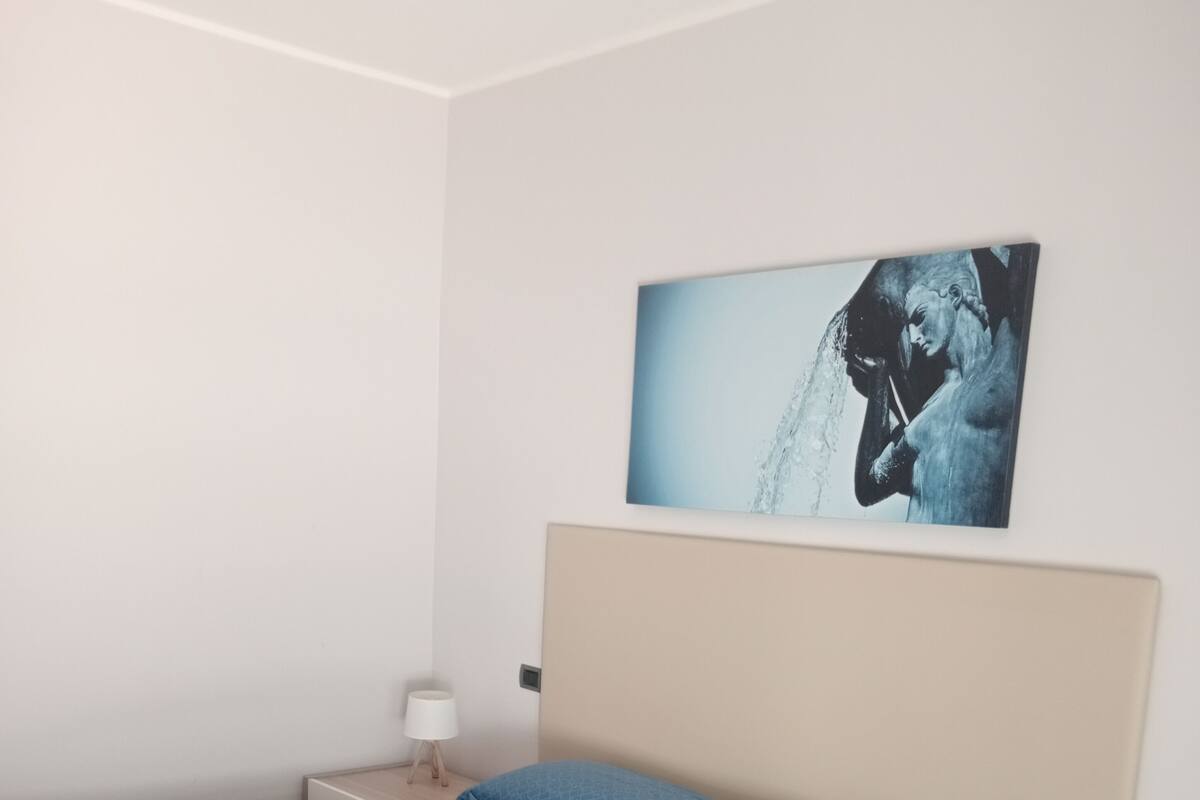 A bedroom with a bed, a nightstand, a lamp, and a painting on the wall.