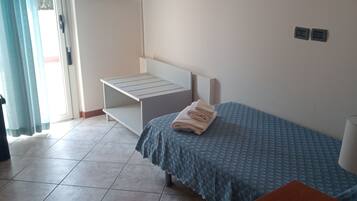 Een slaapkamer met een bed, een bureau, een aan de muur bevestigde televisie en een raam met gordijnen.