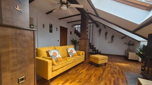 A spacious living area with a yellow sofa, wooden flooring, a ceiling fan, and a staircase. - 1C152: Renovated Triplex in Cimadevilla (Gijón)