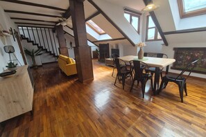 A spacious loft with a wooden floor, a dining area with chairs, a staircase, and a skylight. - 1C152: Renovated Triplex in Cimadevilla (Gijón)