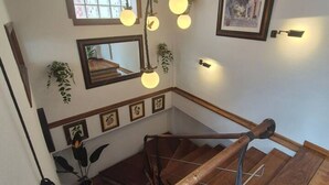 A staircase with wooden railings, a hanging light fixture, framed pictures, and a window with a view. - 1C152: Renovated Triplex in Cimadevilla (Gijón)