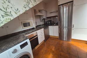 Cocina compacta con lavadora, microondas, refrigerador de acero inoxidable y piso de baldosas.