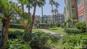 A hotel courtyard with palm trees, a pathway, and colorful buildings in the background.