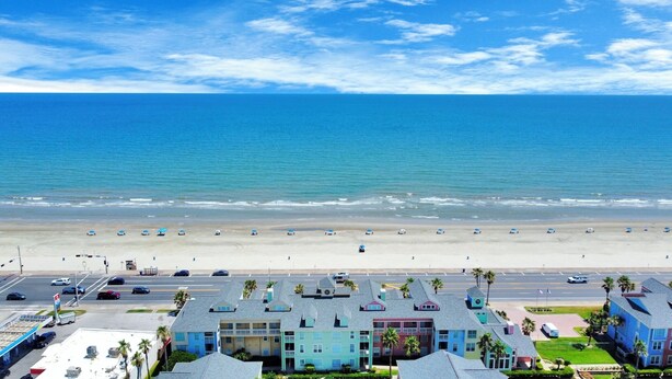 A beachfront hotel with a view of the ocean, a parking lot, and a road with cars.