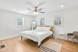 A bedroom with a bed, a ceiling fan, two windows with blinds, a bedside table, a chair, and a rug. - Charming 3BR Retreat in Chamblee (Chamblee)
