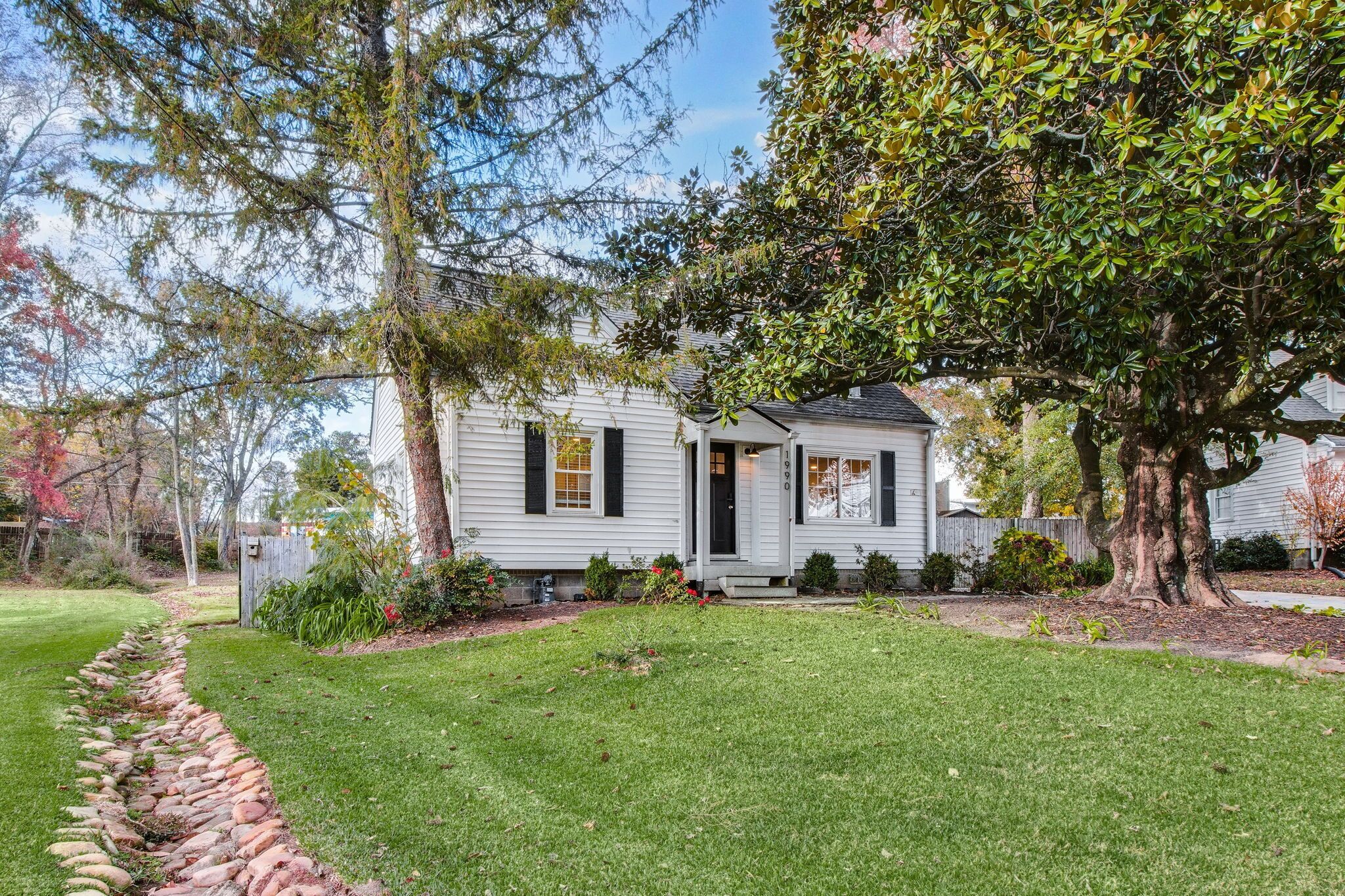 A single-story house with a front porch, a well-maintained lawn, and mature trees.