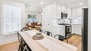 A modern kitchen with white cabinets, a microwave, stove, and refrigerator. There is a dining area with a table and chairs, and a living room with a sofa and coffee table. - Charming 3BR Retreat in Chamblee (Chamblee)