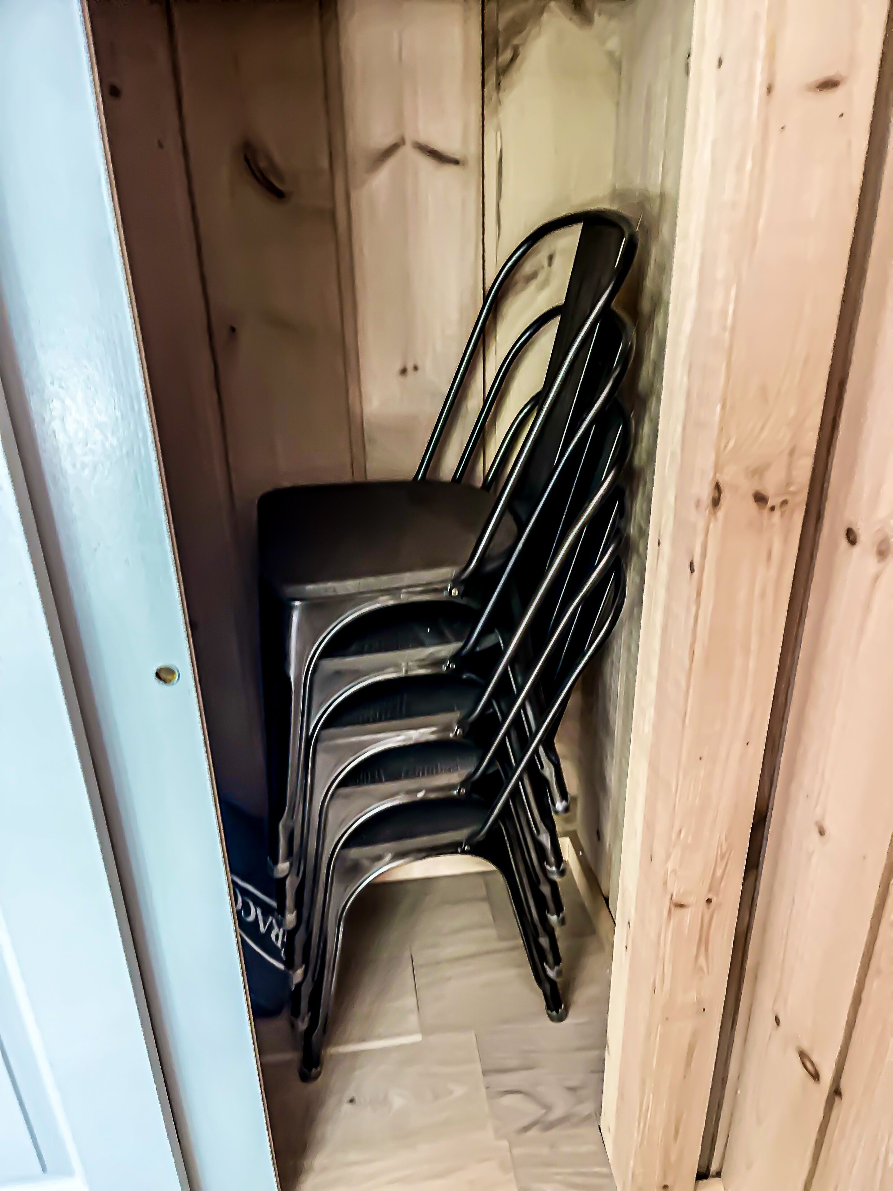 Een hoek van een kamer met een stapel zwarte stoelen en een houten deur.