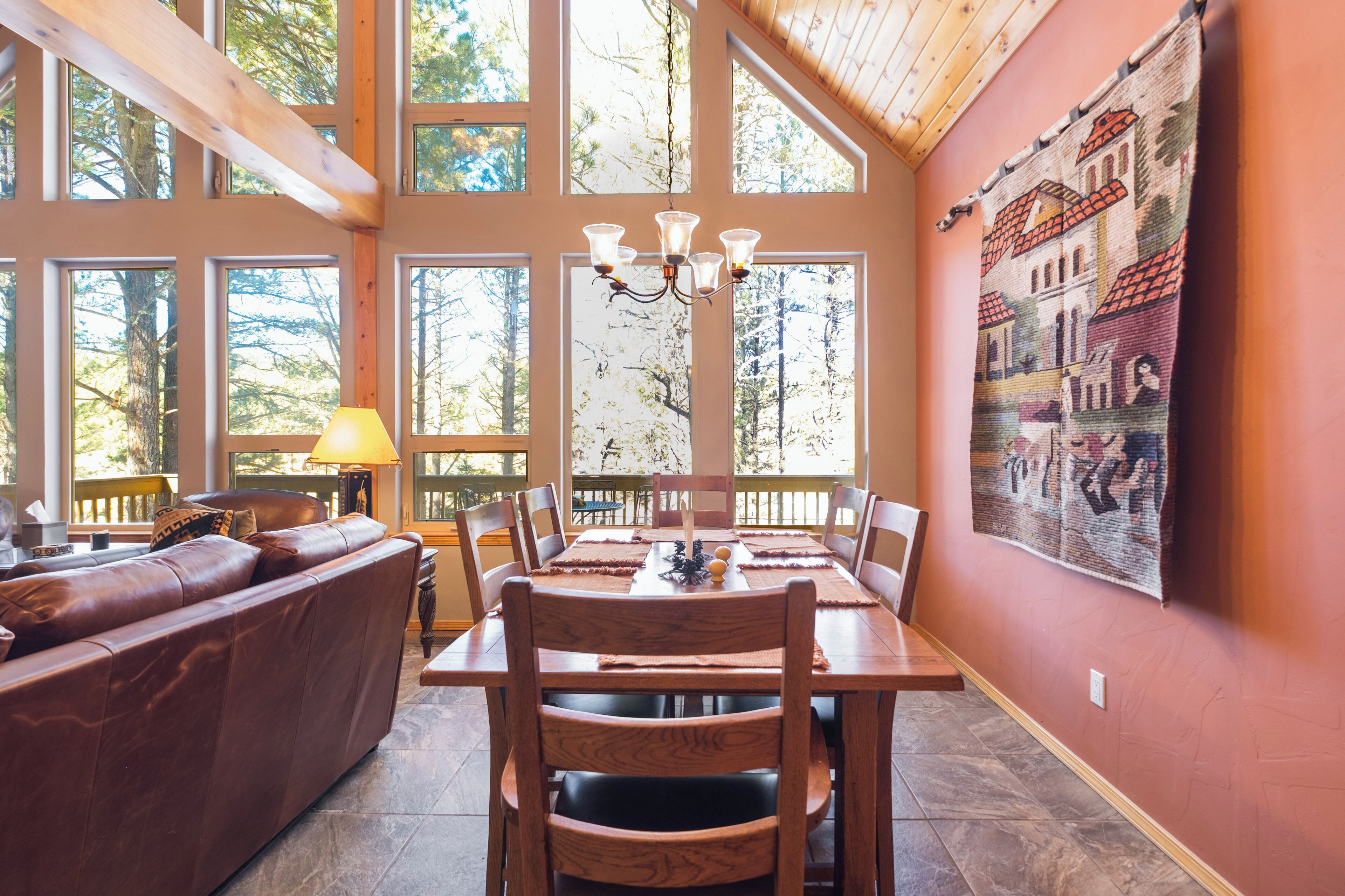 A spacious dining area with a wooden table and chairs, large windows, and a chandelier.