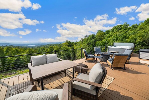 Une terrasse extérieure avec une table et des chaises, un barbecue et une vue panoramique sur une forêt et des montagnes.