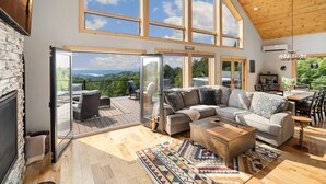 Ein großzügiges Wohnzimmer mit einer großen Eckcouch, einem Kamin und Blick ins Freie durch große Fenster.