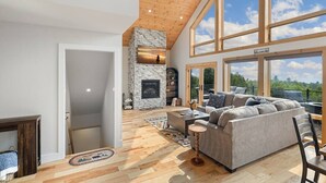 Ein geräumiges Wohnzimmer mit Kamin aus Stein, großen Fenstern und hoher Decke.