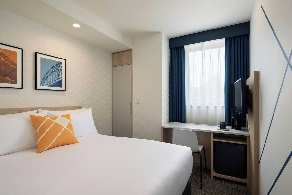 A hotel room with a bed, a desk, a chair, a television, and two framed pictures on the wall.
