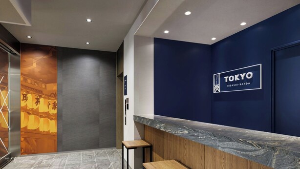 A reception area with a dark blue wall, a marble counter, and two wooden stools. - Four Points Flex By Sheraton Tokyo Higashi Kanda (Tokyo)
