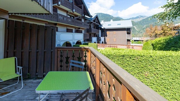 Un edificio de madera con balcones, un césped verde y montañas al fondo.