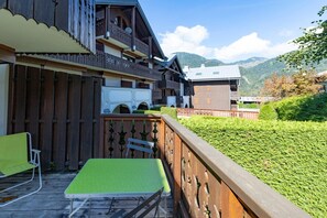A wooden building with balconies, a green lawn, and mountains in the background. - Apartment 'L’Edelweiss Pied des Pistes' with Mountain View and Private Terrace (Morillon)