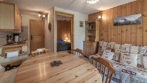 Una habitación acogedora con una mesa de madera para comer, un sofá con cojines estampados, un armario de madera y un cuadro en la pared.