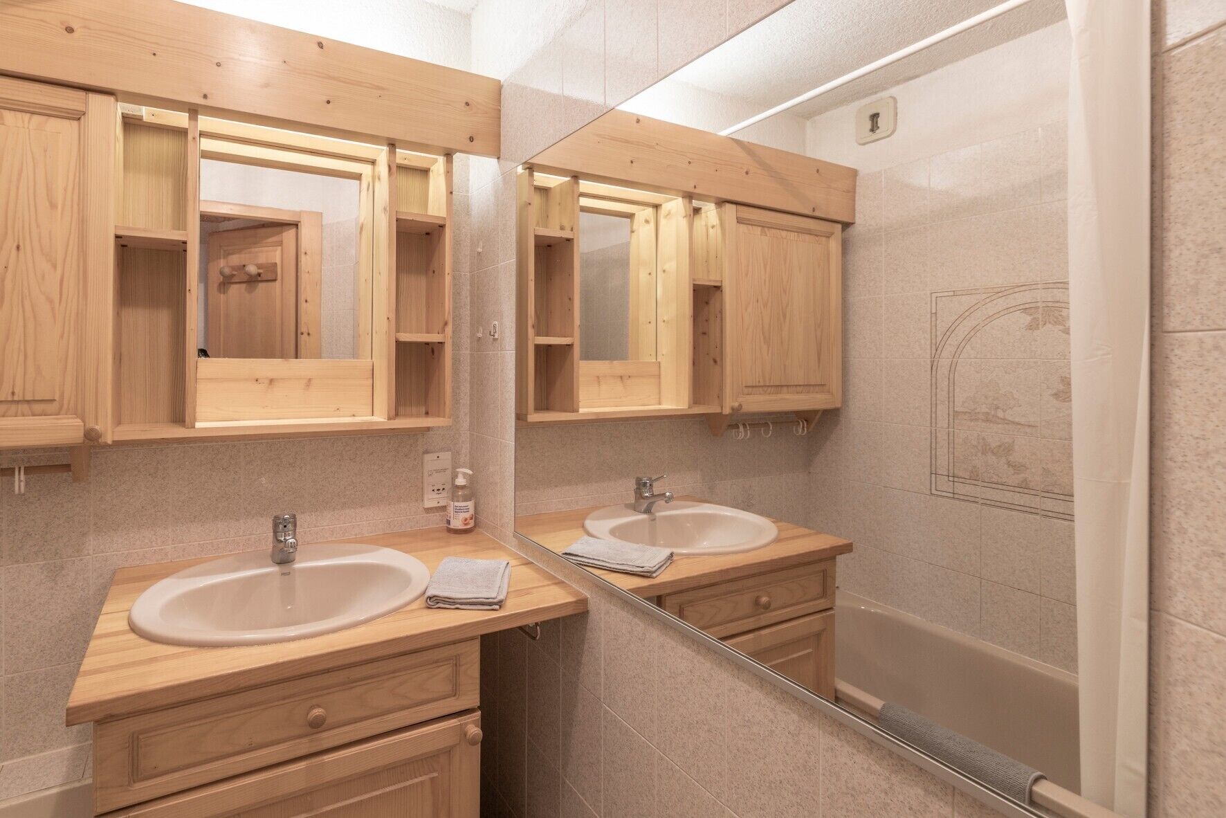 Une salle de bain avec des meubles en bois, deux lavabos, un miroir et une douche.