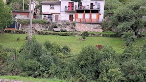 Una casa de dos pisos con un muro de piedra, un pequeño jardín y una terraza de madera.