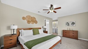 Un dormitorio con cama, mesitas de noche, cómoda, ventilador de techo y una pared decorada.