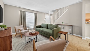 Una sala de estar moderna con un sofá verde, una mesa de centro de madera y una escalera que conduce a un nivel superior.