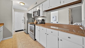 Una cocina moderna con gabinetes blancos, encimera de granito, electrodomésticos de acero inoxidable y una pared decorativa de ladrillo.