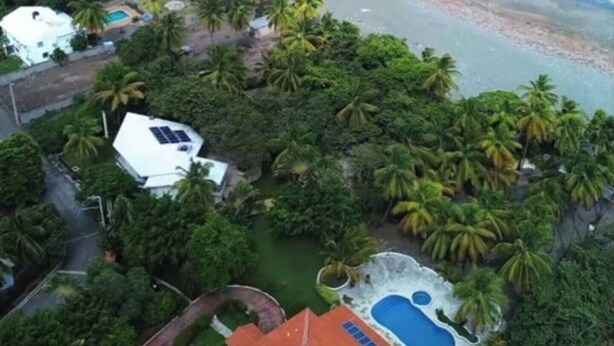 Luchtbeeld van een kustbezit met een zwembad, een strand en weelderige tropische begroeiing.