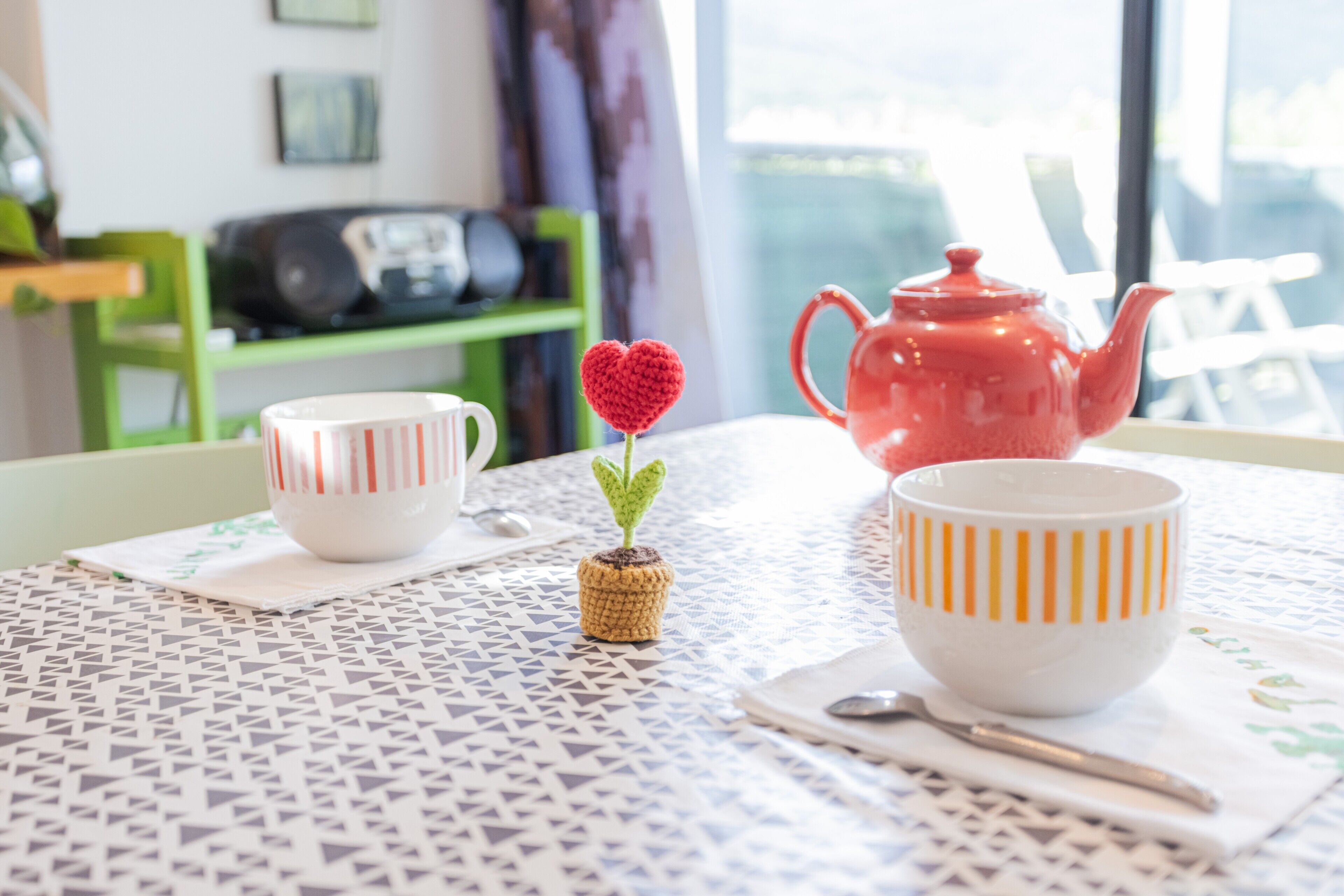 Ein Tisch mit einer Tischdecke mit Muster, eine rote Teekanne und zwei Tassen mit Streifenmuster.