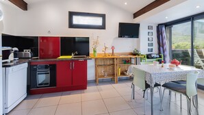 A modern kitchen with red cabinets, a dining area with a table and chairs, and a large window with a view. - F2 holiday home in a corner of paradise with private pool and Wi-Fi (Céret)