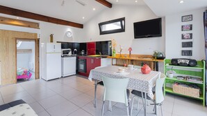 A modern kitchen with a dining area, a TV mounted on the wall, and a green shelf with books. - F2 holiday home in a corner of paradise with private pool and Wi-Fi (Céret)