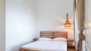 A single bed with a wooden frame, a bedside table, and a hanging lamp.
