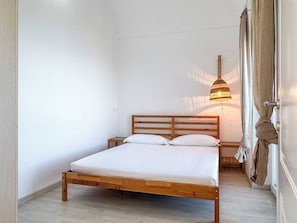 Una cama individual con estructura de madera, una mesita de noche y una lámpara colgante.