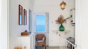 A hallway with a wicker chair, a green vase, and a hanging light fixture.