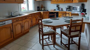 Une cuisine avec des meubles en bois, un pare-feu en carrelage, une table à manger avec des chaises et une fenêtre avec des stores.