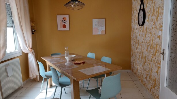 A dining area with a wooden table, blue chairs, a hanging light fixture, and two wall-mounted artworks.